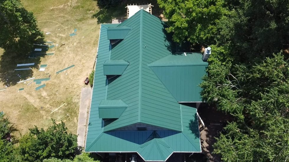 Green standing seam metal roof on residential home with dormers, aerial view