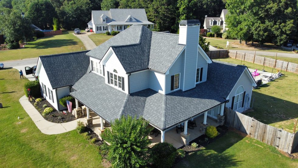 Gray shingle roof on large white farmhouse with covered porch, aerial view